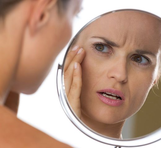 woman looking at skin in the mirror